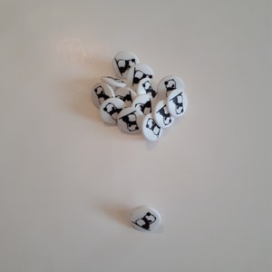 May include: A group of white round buttons with black panda bear designs, scattered on a white surface. One button is separated from the group.