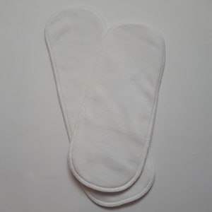 May include: Two white cotton cloth diaper inserts. The inserts are oval shaped and have a white stitched edge.