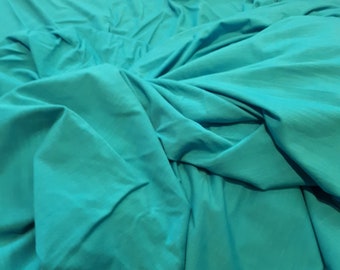 May include: A close-up of a teal fabric with wrinkles and folds. The fabric is smooth and has a soft texture.