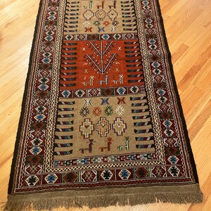 May include: A traditional rug with a brown background and intricate geometric patterns in red, blue, green, and black. The rug features a central design of a tree with stylized branches and leaves.