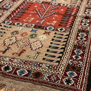 May include: A traditional rug with a beige background and intricate patterns in shades of red, blue, green, and black. The rug has a fringe border and features geometric and floral motifs.
