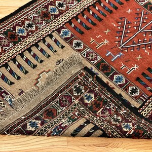 May include: A traditional rug with a geometric pattern in shades of red, black, white, and blue. The rug has a fringe border and is folded in half.