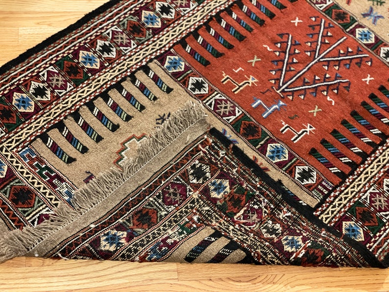 May include: A traditional rug with a geometric pattern in shades of red, black, white, and blue. The rug has a fringe border and is folded in half.
