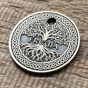 May include: A silver-colored, circular pendant with a tree of life design. The word "FREUJA" is inscribed across the tree. The pendant has a Celtic knot border and a small hole at the top. The Barking Tag Smith is printed at the bottom.
