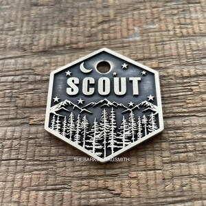 Hexagon-shaped engraved pet ID tag with mountain, forest, moon, and stars design, featuring the name "Scout" in bold lettering. Adventure-themed dog tag handcrafted by The Barking Tagsmith
