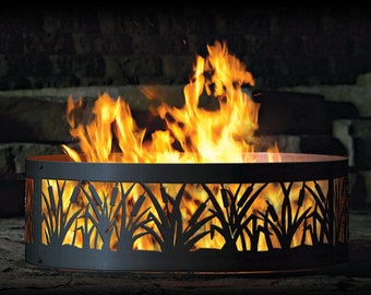 May include: A round, black metal fire pit with a cattail design cut into the sides. Bright orange flames are visible inside the pit. The fire pit is sitting on a stone surface.