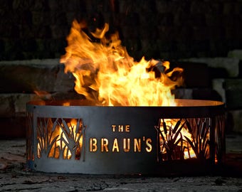 May include: A black metal fire pit with a cutout design of reeds and the text "THE BRAUN'S" in the center. The fire pit is filled with flames.