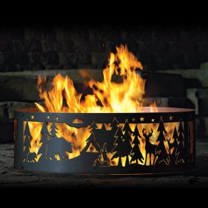Puede incluir: Un pozo de fuego de metal negro con un dise&ntilde;o recortado de una escena de bosque, que incluye &aacute;rboles, un oso, un ciervo y estrellas. El pozo de fuego est&aacute; lleno de llamas.