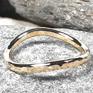 May include: A hammered gold band ring with a rounded, slightly curved shape.