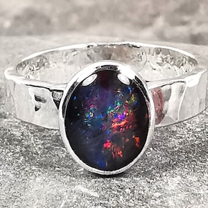 Könnte beinhalten: Ein Silberring mit einem gehämmerten Band und einem großen ovalen schwarzen Opal-Edelstein.