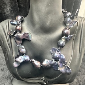 May include: A necklace made of iridescent black pearls. The pearls are strung together in a loose, flowing style. The necklace is displayed on a black mannequin bust.