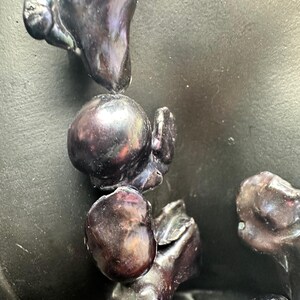 May include: A close-up of a strand of black pearls with iridescent hues. The pearls are various shapes and sizes, some round and some more irregular. The pearls are arranged in a cascading pattern.