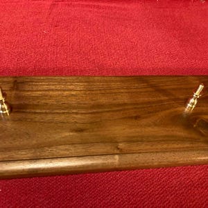 May include: A wooden wall-mounted key holder with two brass hooks. The wood has a dark brown stain and a natural wood grain pattern.