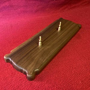 May include: A wooden plaque with a dark walnut finish and two brass knobs. The plaque has a decorative edge and is perfect for displaying a collection of items.