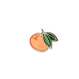 Könnte beinhalten: Eine goldfarbene Emaille-Anstecknadel mit einer Cartoon-Orange mit grünen Blättern. Die Orange ist hellorange mit einem dunkleren orangenfarbenen Umriss. Die Blätter sind dunkelgrün mit einem helleren grünen Umriss.