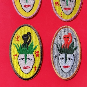 May include: Six embroidered iron-on patches with a yellow background and a white face with black eyes and red lips. Each patch features a green plant with a black or red animal on top. The Japanese text on the patches reads: "上こう", "出し", "かし", "けんた", "小んた", and "あ"