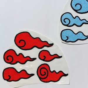 May include: Two sets of cloud-shaped patches. One set features red clouds with black outlines, and the other set has blue clouds with black outlines. The patches are on a white background.
