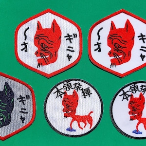 以下が含まれることがあります： 赤い猫と黒い猫の漫画が描かれた刺繍パッチが5つ。各パッチには日本語で「Su-Ki-Ya」と書いてあります。パッチは円形、六角形、丸みを帯びた正方形など、さまざまな形をしています。