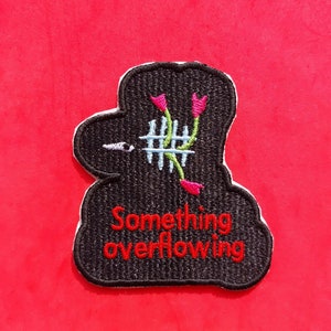 May include: Embroidered patch with a black outline and a white border. The patch features a stylized design of a head with a fence and flowers, with the words "Something overflowing" in red.