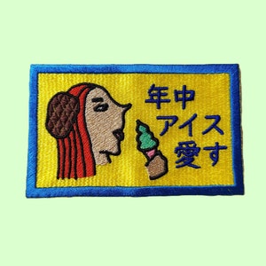 Peut inclure: Un patch brodé jaune avec une femme de dessin animé aux cheveux roux mangeant un cornet de glace vert. Le texte sur le patch est "年中アイス愛す".