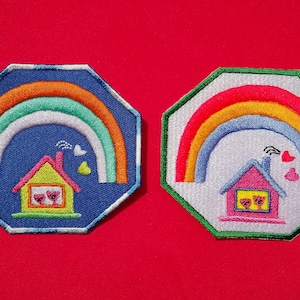 May include: Two embroidered patches with a rainbow and a house with hearts. The rainbow is in shades of orange, yellow, blue, and green. The house is yellow with a red roof and white windows. The patches are octagonal and have a white background.
