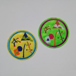 K&ouml;nnte beinhalten: Zwei runde gestickte Aufn&auml;her mit bunten geometrischen Mustern. Die Aufn&auml;her befinden sich auf einem wei&szlig;en Hintergrund.