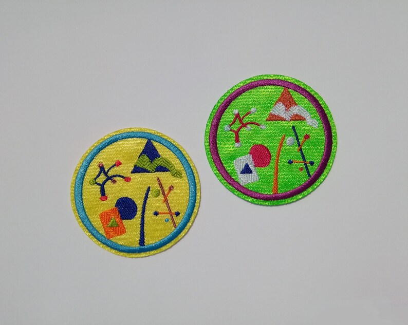 K&ouml;nnte beinhalten: Zwei runde gestickte Aufn&auml;her mit bunten geometrischen Mustern. Die Aufn&auml;her befinden sich auf einem wei&szlig;en Hintergrund.