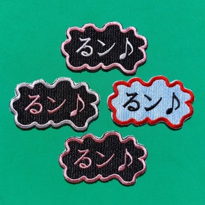 Puede incluir: Cuatro parches bordados en forma de nubes con la palabra japonesa "run" y una nota musical en negro, rosa y azul.