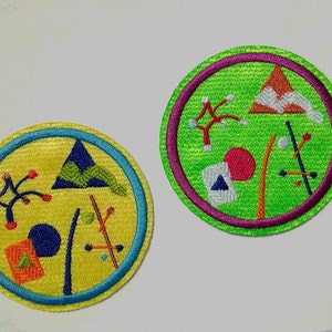 Może przedstawiać: Dwa haftowane naszywki z geometrycznymi kształtami i abstrakcyjnymi wzorami. Jedna naszywka jest żółta z niebieskim obramowaniem, a druga zielona z fioletowym obramowaniem.