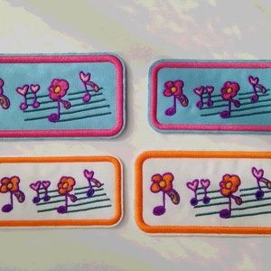 Könnte beinhalten: Vier gestickte Bügelbilder mit Noten und Blumen. Zwei Patches sind hellblau mit rosa Rändern und zwei Patches sind weiß mit orangefarbenen Rändern.