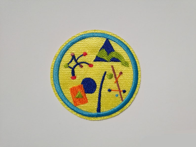 K&ouml;nnte beinhalten: Ein gelber gestickter Aufn&auml;her mit blauem Rand. Der Aufn&auml;her zeigt ein stilisiertes Design eines Berges, eines Baumes, eines Zeltes und anderer geometrischer Formen.