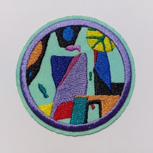 May include: A round, embroidered patch with a colorful abstract design. The patch features a variety of shapes and colors, including purple, blue, green, yellow, orange, and red. The patch is surrounded by a purple border.