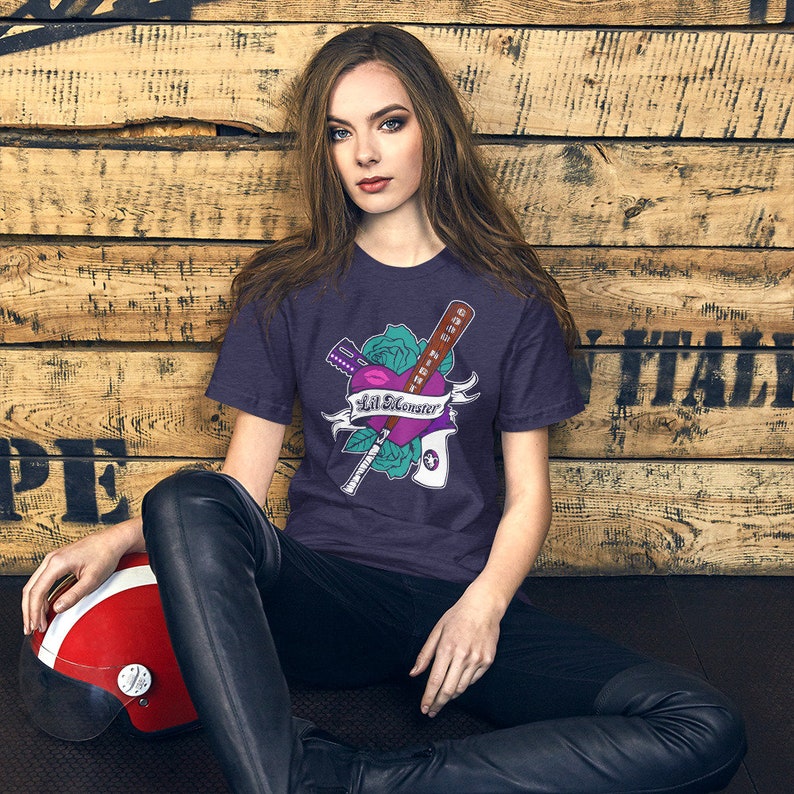 K&ouml;nnte beinhalten: Ein lila T-Shirt mit einem Aufdruck eines Herzens mit einem Baseballschl&auml;ger, einem Messer und einer Rose. Der Text auf dem Shirt lautet "Lil Monster".