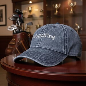 Blue vintage dad hat with embroidered “he’s golfing” design, adjustable baseball cap for golf wife, country club style women’s golf hat