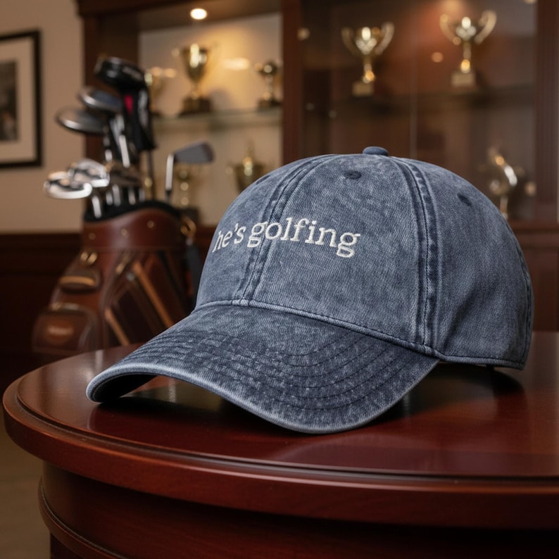Blue vintage dad hat with embroidered “he’s golfing” design, adjustable baseball cap for golf wife, country club style women’s golf hat