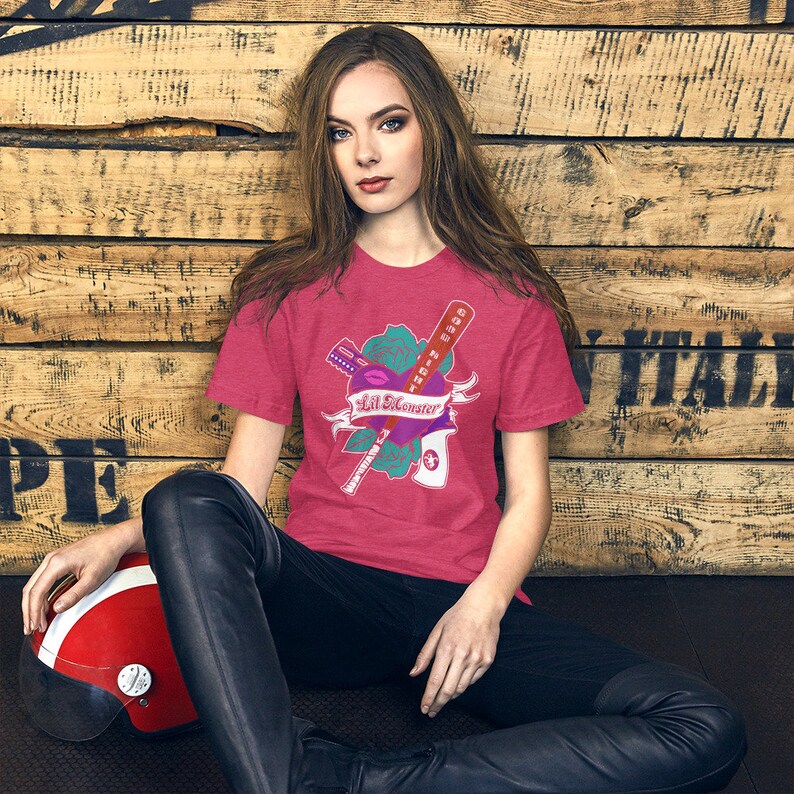 K&ouml;nnte beinhalten: Eine Frau tr&auml;gt ein pinkfarbenes T-Shirt mit einem Motiv einer Rose, einem Baseballschl&auml;ger, einem Lippenstift und dem Text "Lil Monster".