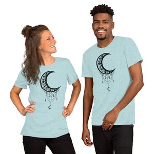 May include: Two people wearing light blue t-shirts with a black crescent moon design. The moon is adorned with intricate details and dangling charms.