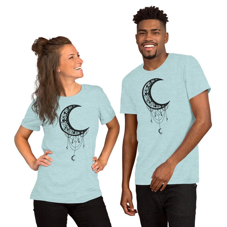May include: Two people wearing light blue t-shirts with a black crescent moon design. The moon is adorned with intricate details and dangling charms.