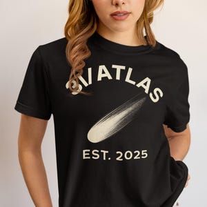 May include: Black t-shirt featuring the word "ATLAS" in white, arched above a cream-coloured brushstroke. Below, the text "EST. 2025" is printed in white. The shirt has a crew neck design.