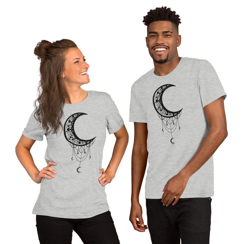 May include: Two grey t-shirts with a black crescent moon design. The moon is adorned with intricate details and dangling chains. The design is centered on the front of each shirt.