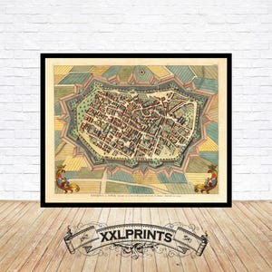 Puede incluir: Impresión enmarcada de un mapa antiguo de una ciudad, con calles y edificios detallados en un estilo antiguo y colorido. El mapa está rodeado de campos y fortificaciones, con elementos decorativos en las esquinas. La impresión se muestra sobre un suelo de madera.