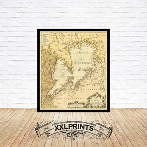 May include: Framed vintage map print with a black border. The map features a detailed depiction of a coastal region, with text in the center reading "Western". The map is set against a cream-coloured background. The print is displayed on a white brick wall.