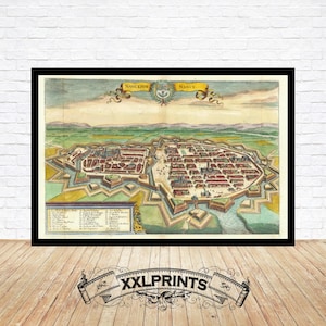 May include: A framed vintage map of Nancy, France, in a detailed, colorful illustration. The map shows the city's layout with buildings, fortifications, and surrounding landscape. The map is in a black frame and is displayed on a wooden floor.
