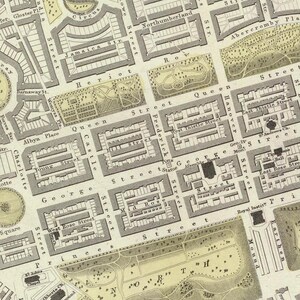 May include: A vintage map of a city with streets and buildings labeled. The map is printed in black and white on a cream-colored background. The map shows the layout of the city with streets, parks, and buildings.