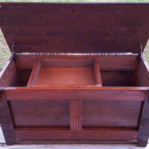 Puede incluir: Un cofre de almacenamiento de madera marr&oacute;n oscuro con una tapa con bisagras y un interior dividido. El cofre tiene un dise&ntilde;o sencillo con un panel elevado en la parte delantera.