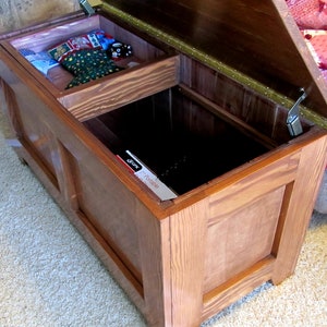 Puede incluir: Un cofre de almacenamiento de madera con una tapa con bisagras y un compartimento m&aacute;s peque&ntilde;o en el interior. El cofre est&aacute; abierto y la tapa est&aacute; levantada. El cofre est&aacute; hecho de madera marr&oacute;n claro con un acabado natural.