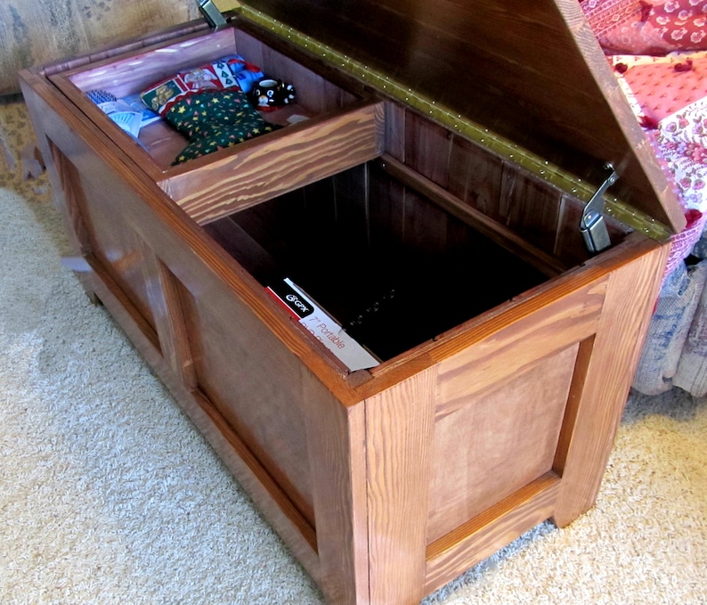 Puede incluir: Un cofre de almacenamiento de madera con una tapa con bisagras y un compartimento m&aacute;s peque&ntilde;o en el interior. El cofre est&aacute; abierto y la tapa est&aacute; levantada. El cofre est&aacute; hecho de madera marr&oacute;n claro con un acabado natural.