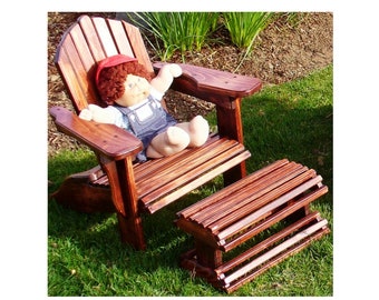 May include: A wooden adirondack chair with a footrest, both stained a dark brown. A doll wearing a red hat and overalls is sitting in the chair.