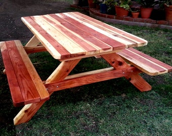 May include: A wooden picnic table with two benches. The table top is made of natural wood with a reddish-brown stain. The benches are also made of natural wood with a reddish-brown stain.