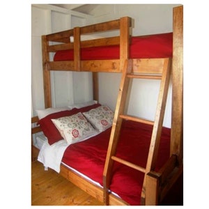 May include: A wooden bunk bed with a red mattress on the top bunk and a red duvet on the bottom bunk. The bed has a ladder on the side.